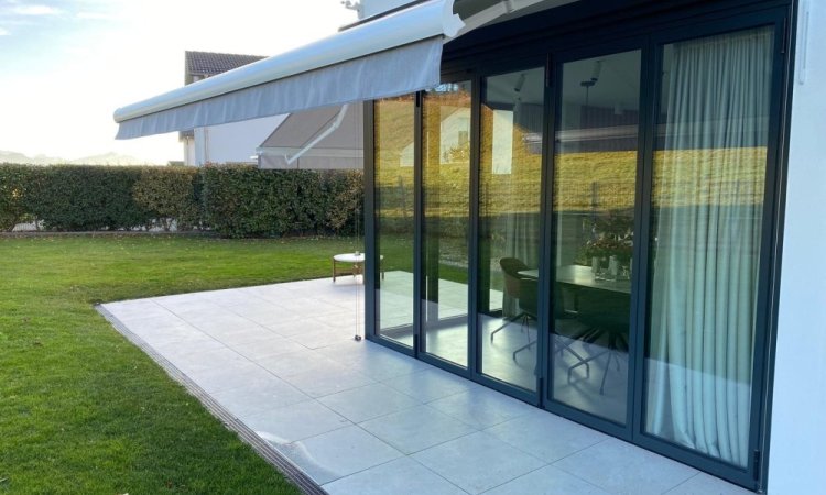 Splendide extension de pièce de vie réalisée grâce à une baie accordéon d’angle, offrant une ouverture maximale sur l’extérieur.